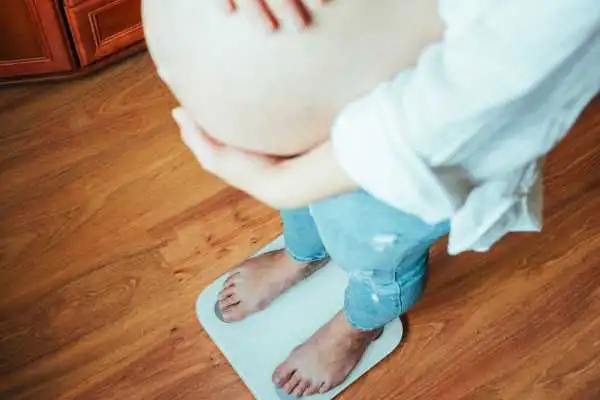 Image of woman weighing herself and experiencing weight gain through pregnancy Bishopbriggs