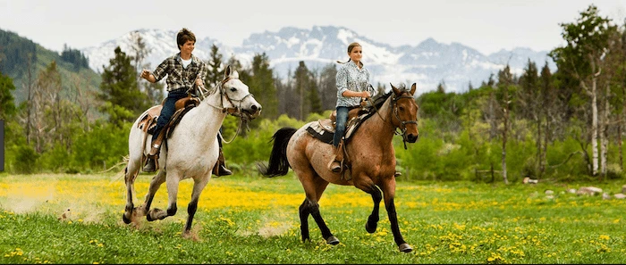 Confident plus-size woman riding Bishopbriggs a horse through a field with a smile on her face.
